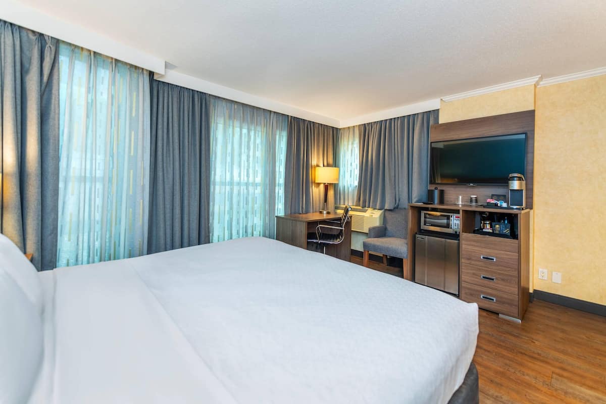 Une chambre d’hôtel avec un grand lit, un bureau avec une lampe, une télévision et un minibar.