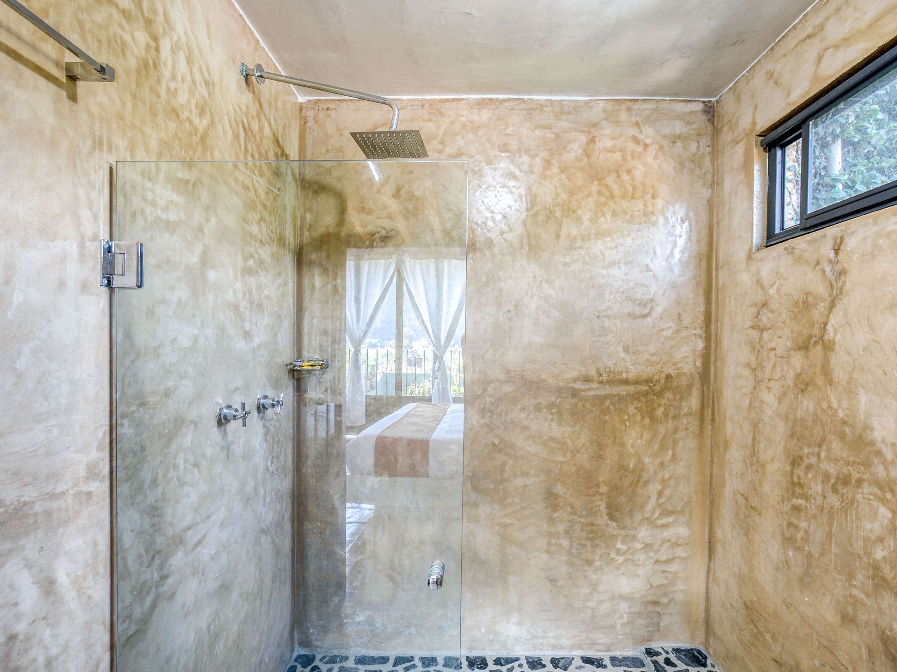 Una ducha con cerramiento de vidrio, un cabezal de ducha de mano, una puerta de cristal y una ventana con cortinas.