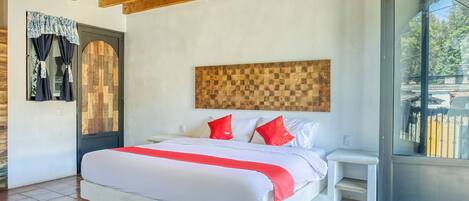 A bedroom with a large bed, a wooden ceiling, a small bedside table, and a view through a glass door.
