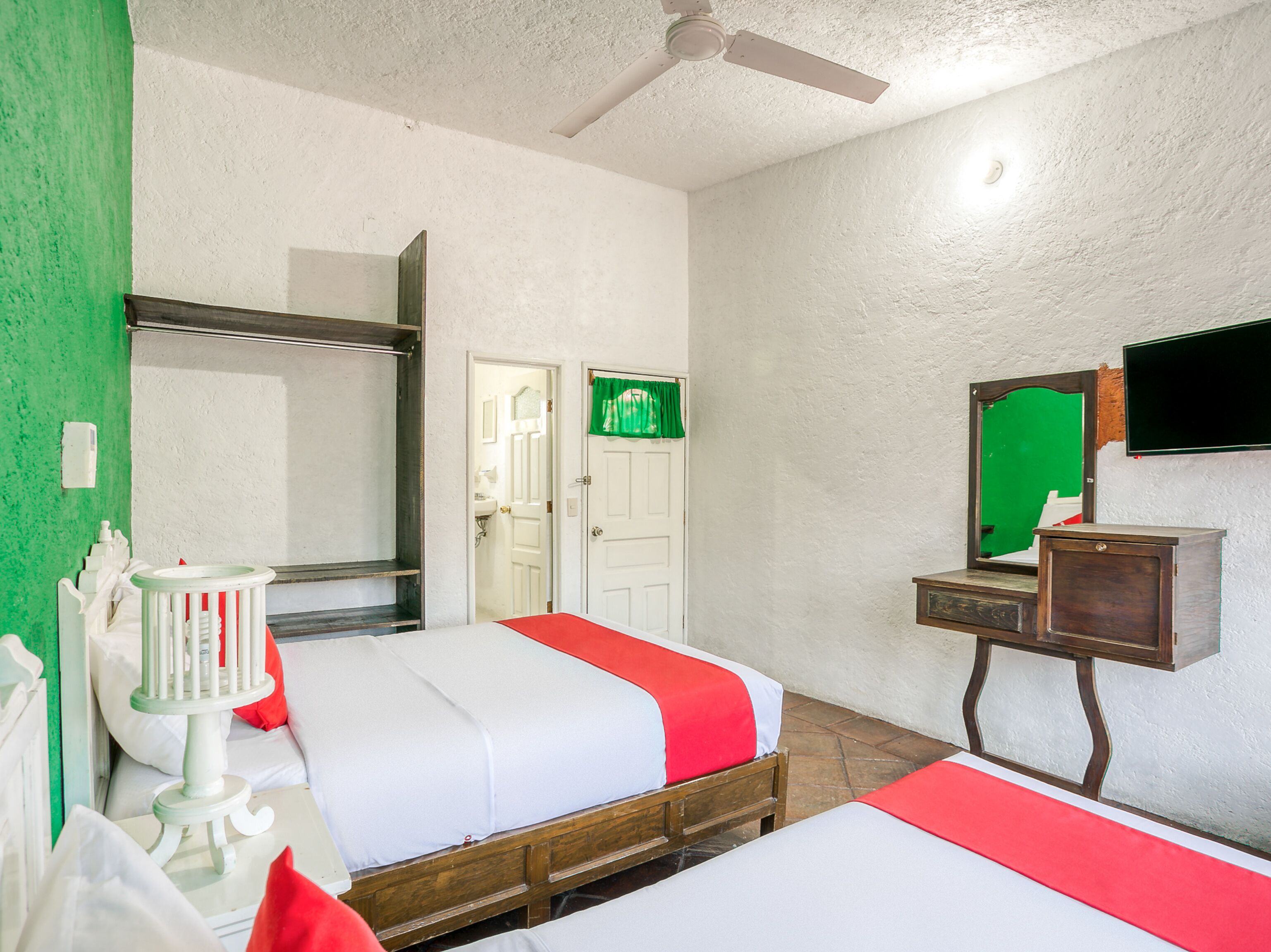A hotel room with two beds, a ceiling fan, a mirror, a television, and a small wooden cabinet.