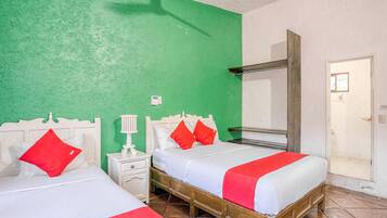 Una habitación con dos camas, cada una con ropa de cama blanca y detalles en rojo, una mesita de noche pequeña con lámpara y un espejo sobre las camas.