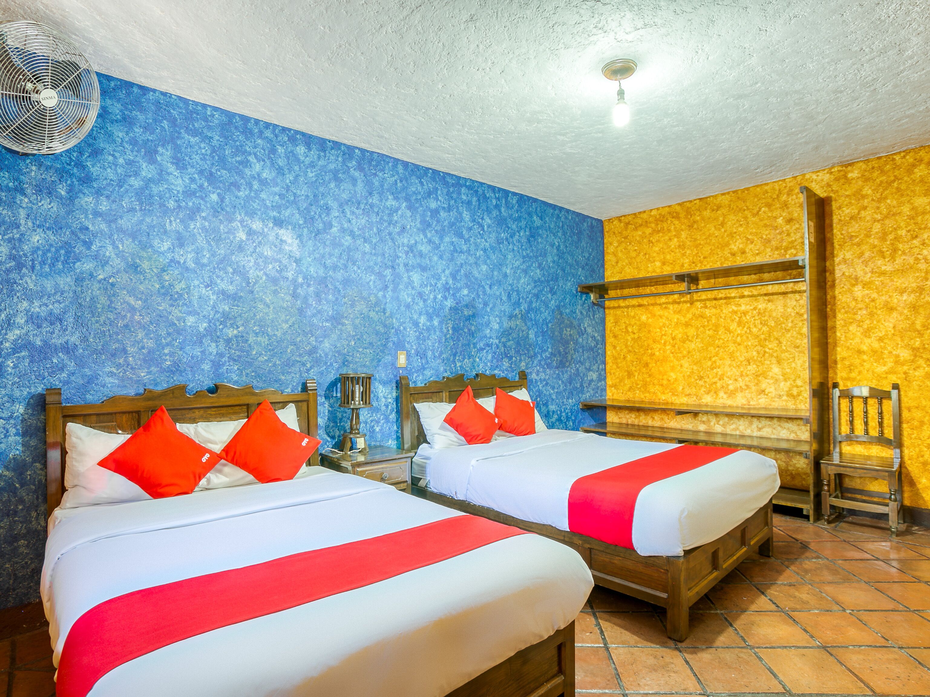 Habitación de hotel con dos camas, cada una con ropa de cama roja y blanca, cabeceros de madera y mesitas de noche con lámparas.