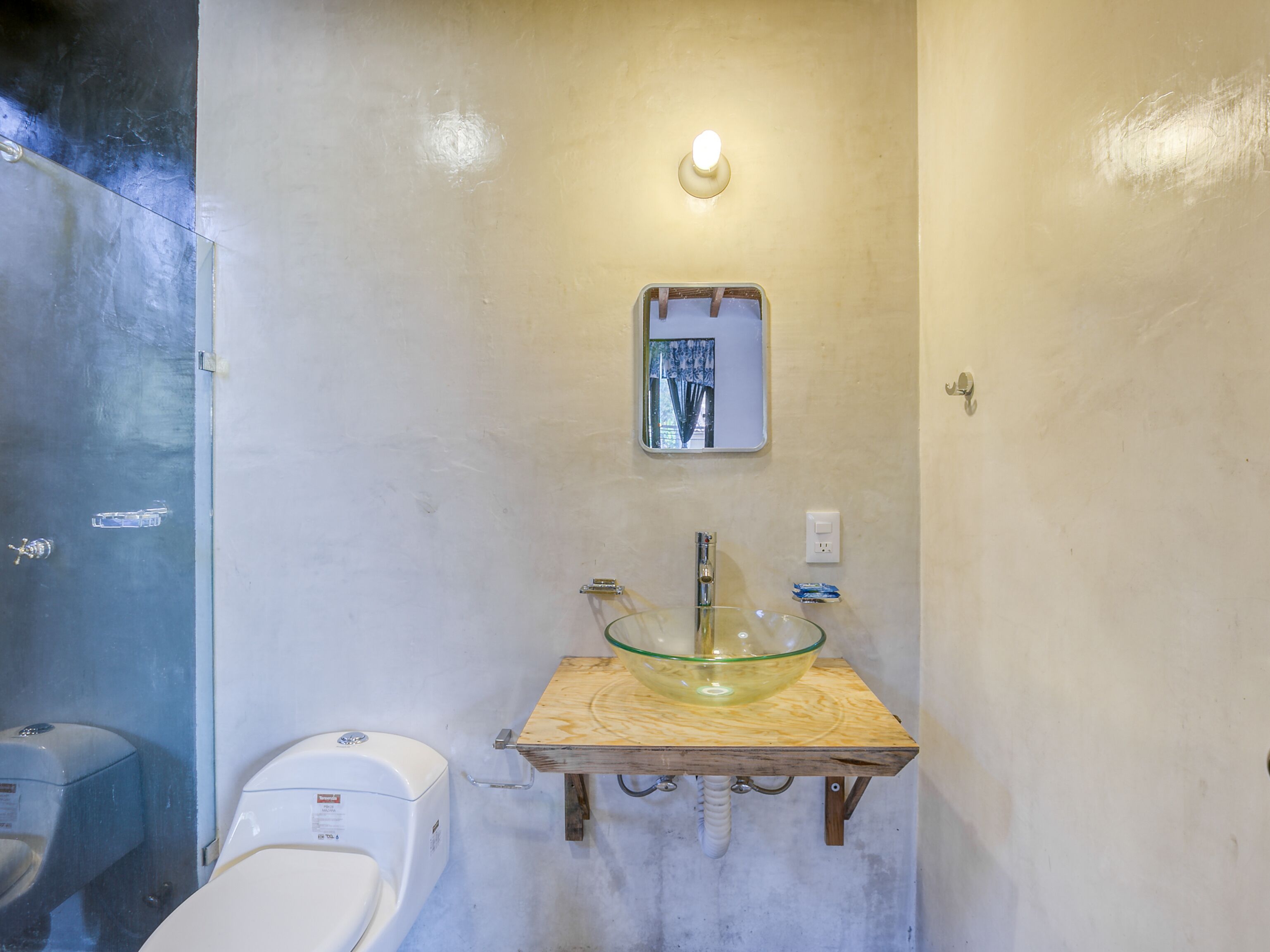 Un baño con un lavabo de cristal sobre una repisa de madera, un inodoro blanco y un espejo con luz superior.