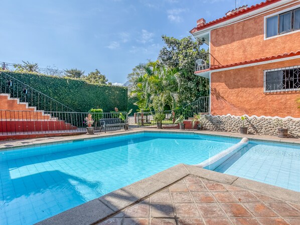 Enjoy a refreshing swim in the pool surrounded by lush greenery and a balcony.