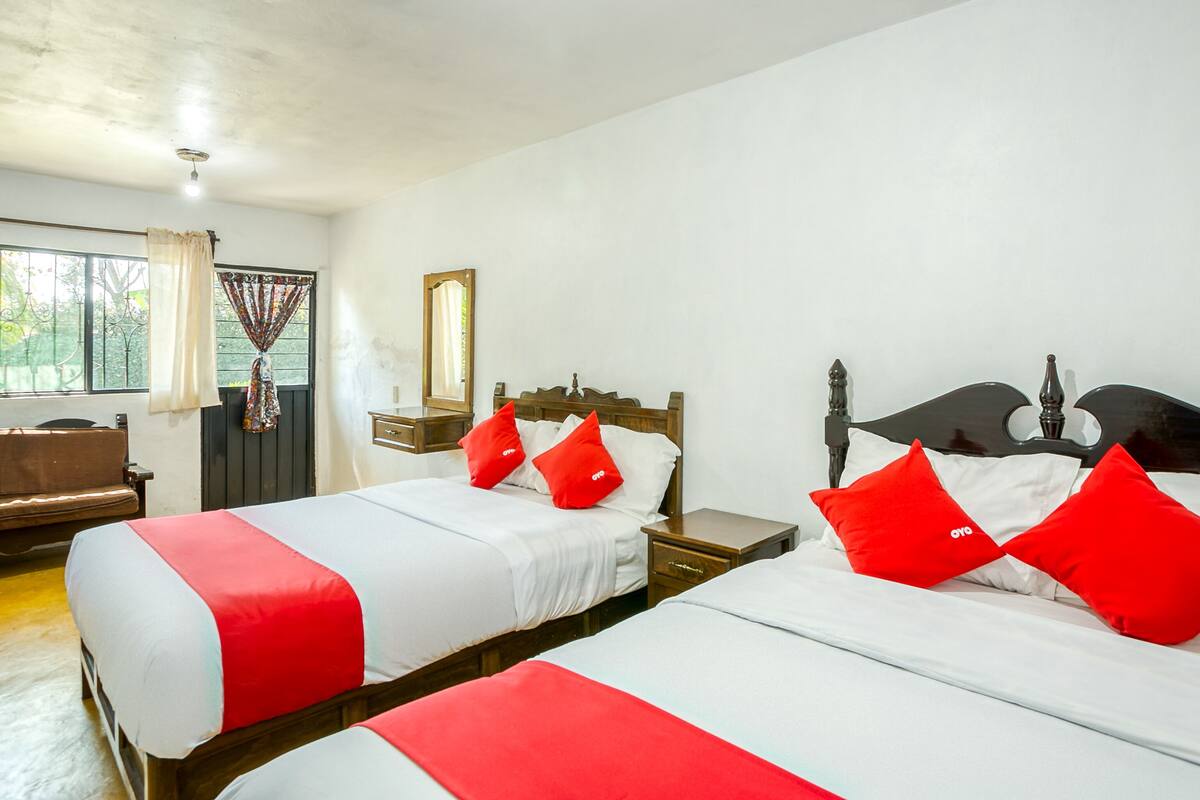 Ein Hotelzimmer mit zwei Betten, einem hölzernen Kopfteil, einem Nachttisch, einem Spiegel und einem Fenster mit Vorhängen.