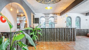 Zona de recepción con mostrador de piedra, plantas en macetas y techo decorativo.