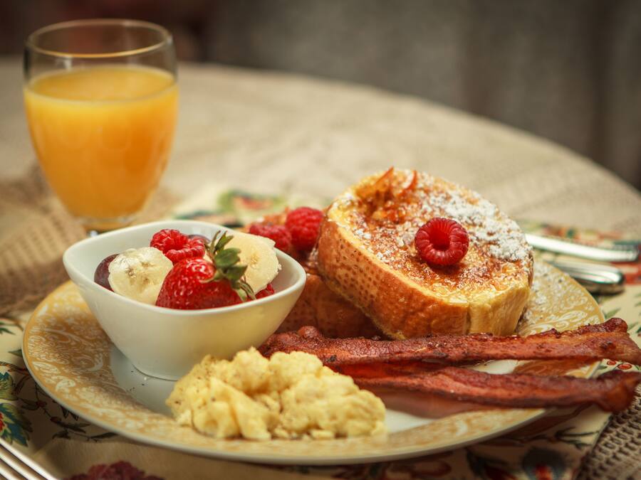 A breakfast plate with toast, strawberries, raspberries, a bowl of yogurt, and a glass of orange juice.