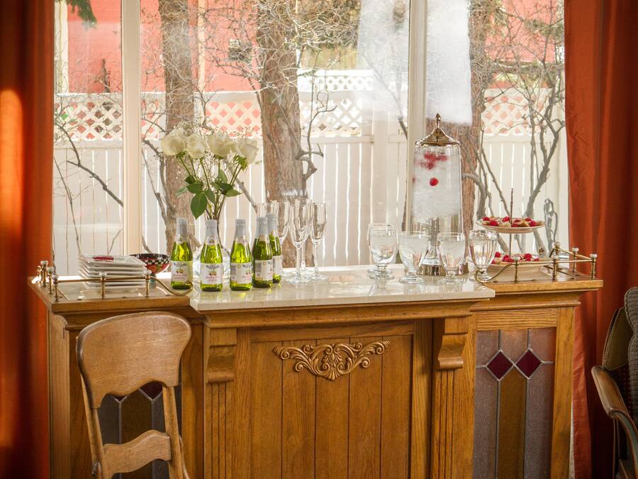 Un comptoir en bois avec un tabouret, une fenêtre avec des rideaux et une vue sur des arbres et une clôture.