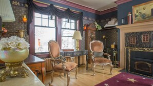 Ein Zimmer mit zwei verzierten Stühlen, einem Kamin und einer großen Vase mit Blumen auf einem Tisch.