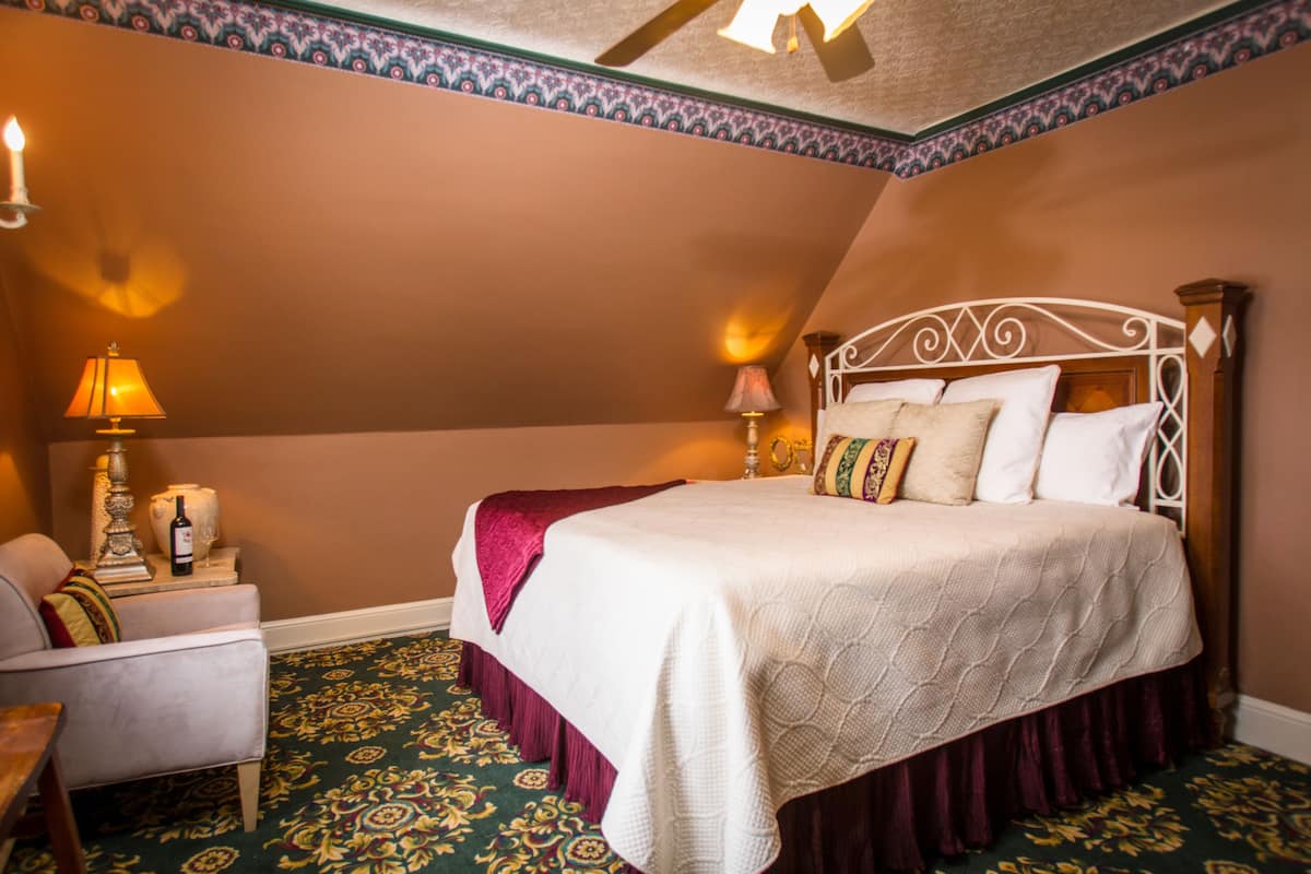 A bedroom with a bed, two bedside lamps, a chair, and a decorative vase.