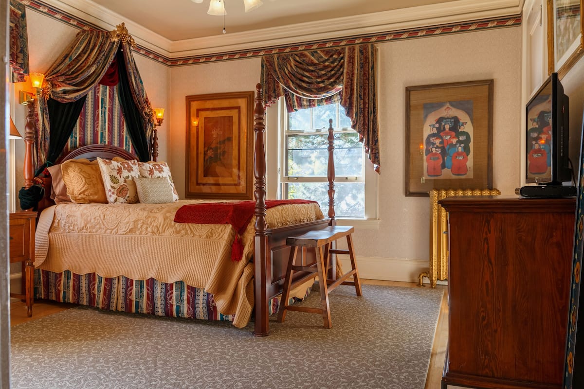 A traditional bedroom with a four-poster bed, a wooden nightstand, a bench, and a dresser.
