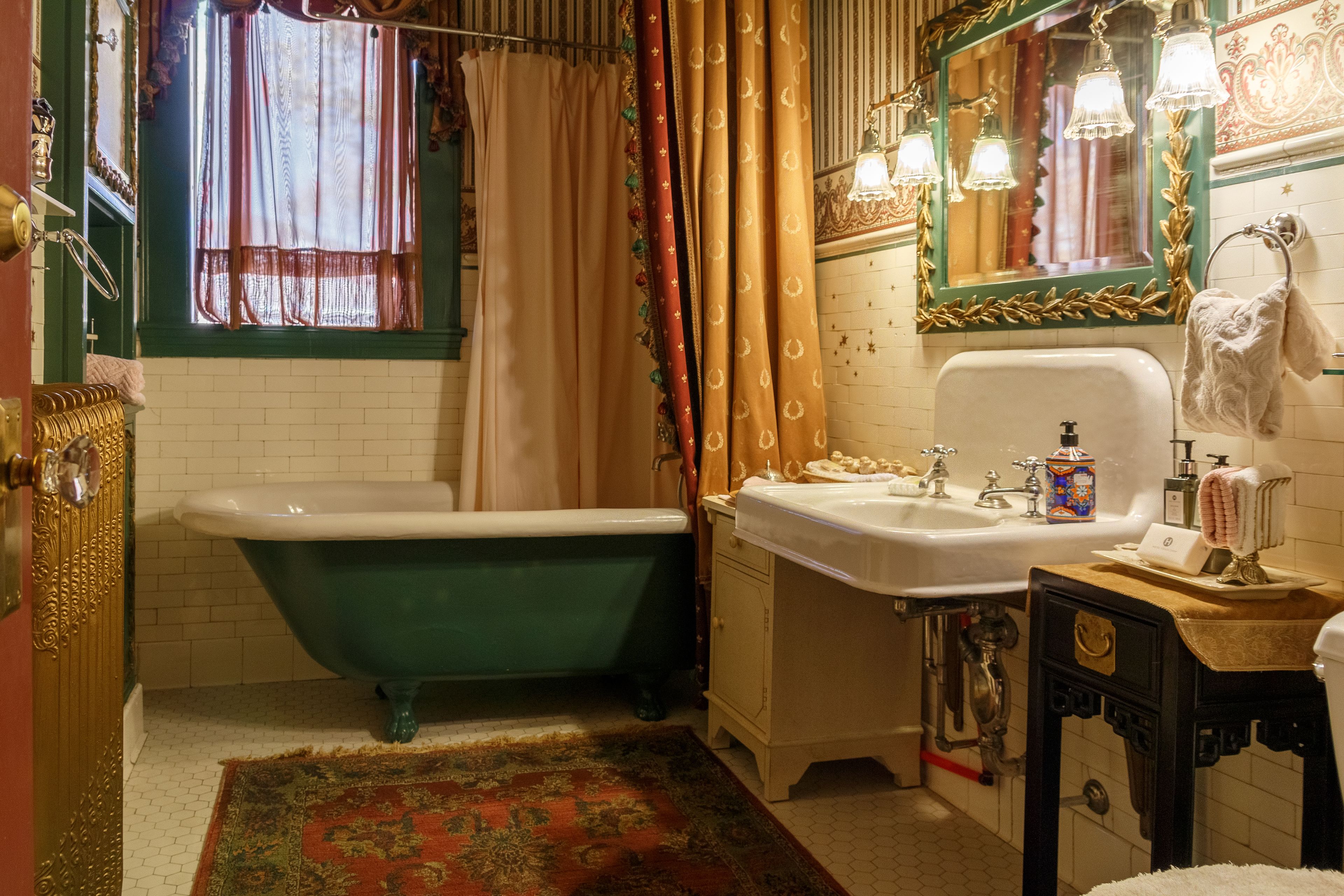 A vintage bathroom with a green clawfoot bathtub, a white sink, and a mirror with ornate gold trim.