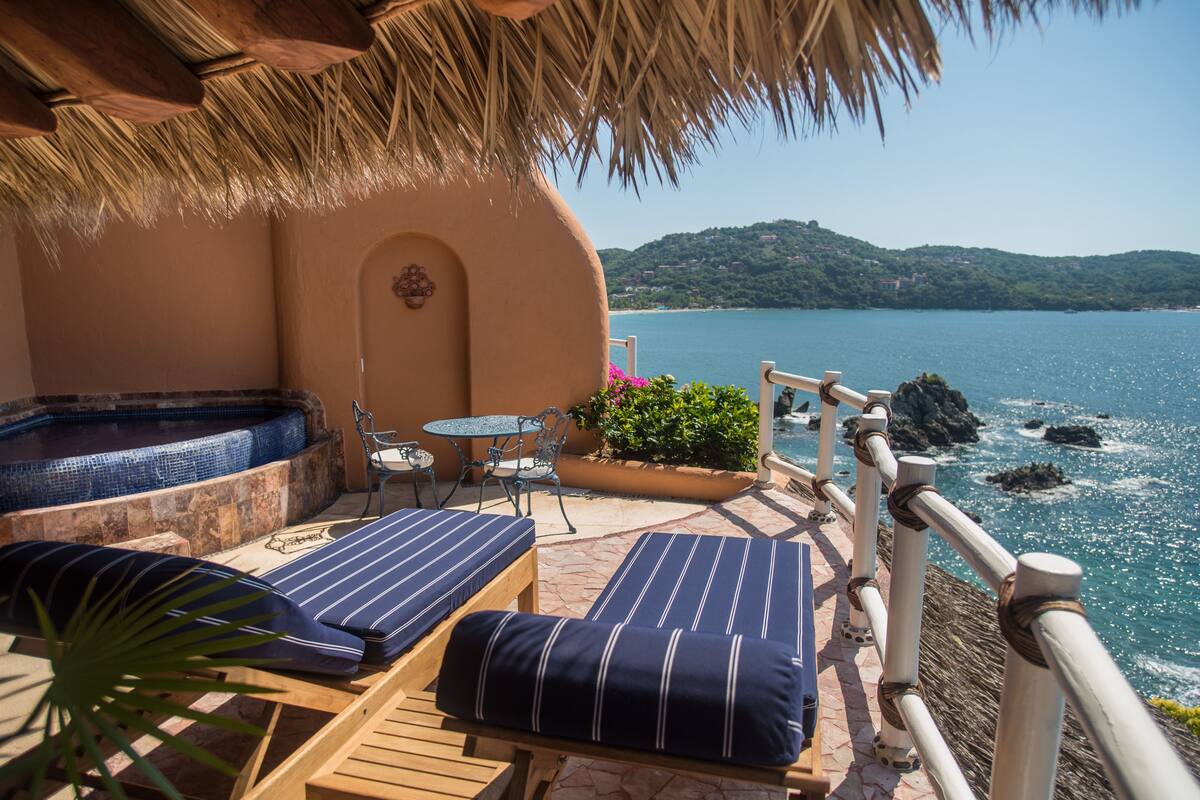 A terrace with two striped lounge chairs, a small table, and a hot tub.
