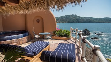 A terrace with two striped lounge chairs, a small table, and a hot tub.