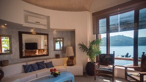 Un salón con un sofá blanco, una mesa de centro azul y un ventanal con vistas al mar.