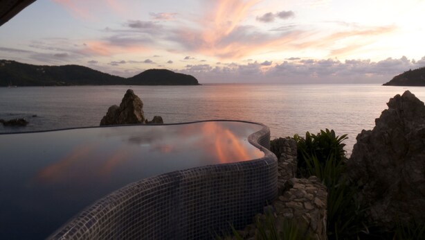 Una piscina infinita con vistas al mar y colinas lejanas.