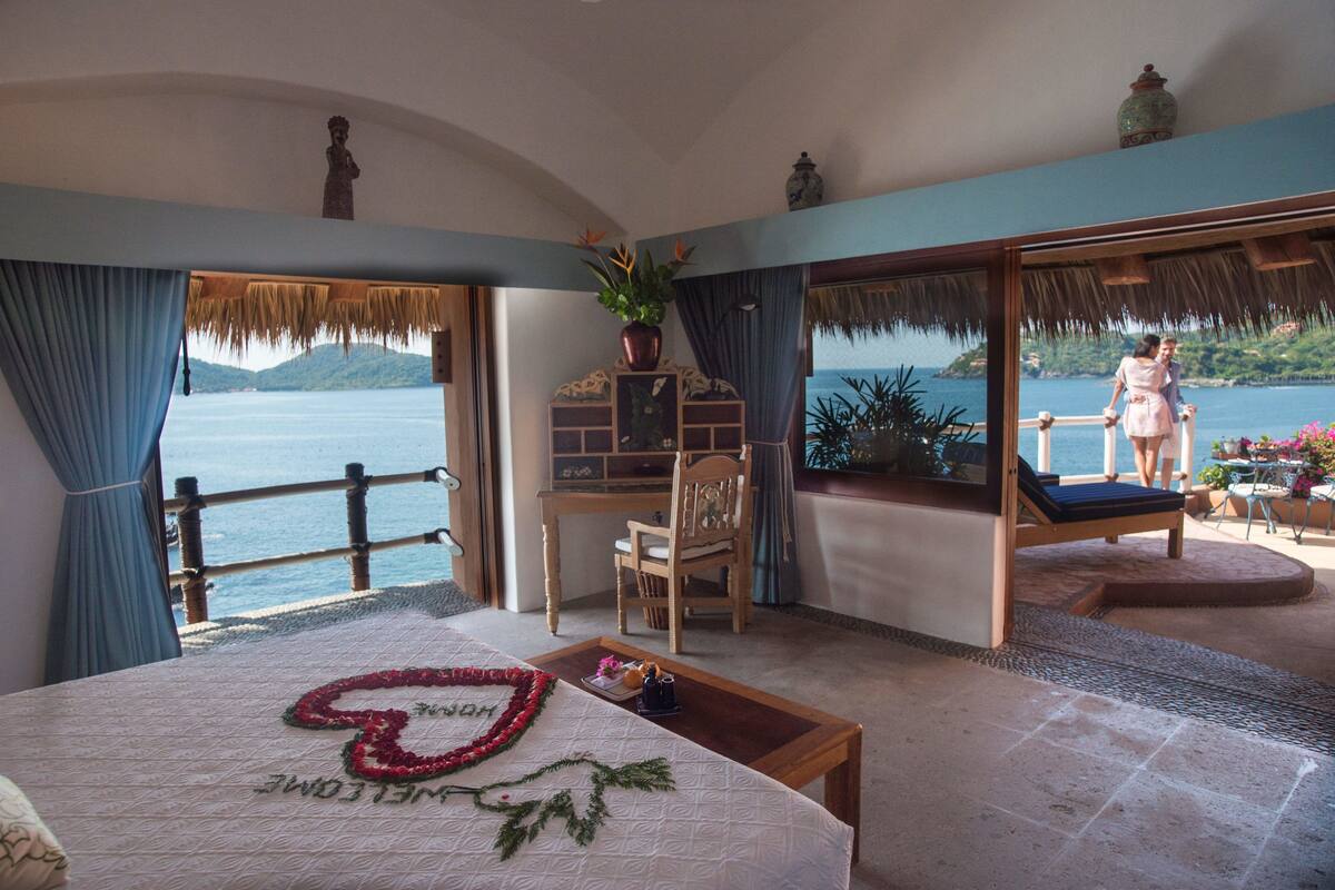 A bedroom with a large bed, a desk, and a view of the sea.