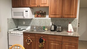 A kitchen with wooden cabinets, a white stove, a microwave, a sink, and a toaster. - Sunshine LA BnB (Van Nuys)