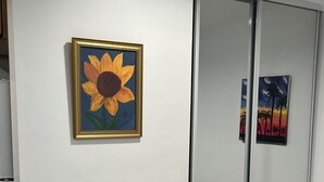 A room with a sliding glass door closet, a framed painting of a sunflower, and a bed with striped bedding. - Sunshine LA BnB (Van Nuys)
