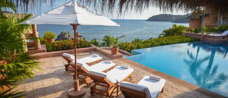 A poolside area with lounge chairs and a thatched umbrella, overlooking a body of water.