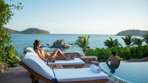 A poolside area with lounge chairs and a pool, overlooking a body of water and greenery. - Villa El Ensueño by La Casa Que Canta (Zihuatanejo)