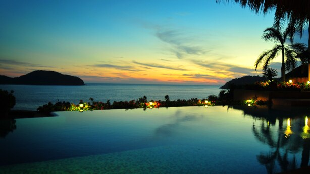 A poolside view with a sunset over the water, palm trees, and a distant island. - Villa El Ensueño by La Casa Que Canta (Zihuatanejo)