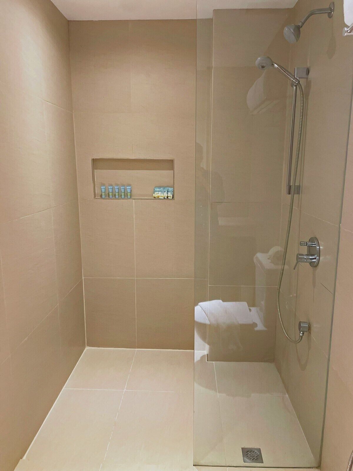 A glass-enclosed shower with a handheld showerhead and a wall-mounted faucet.