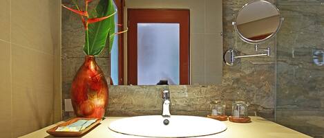A bathroom with a white sink, a mirror, a vase with a plant, and a trash bin.