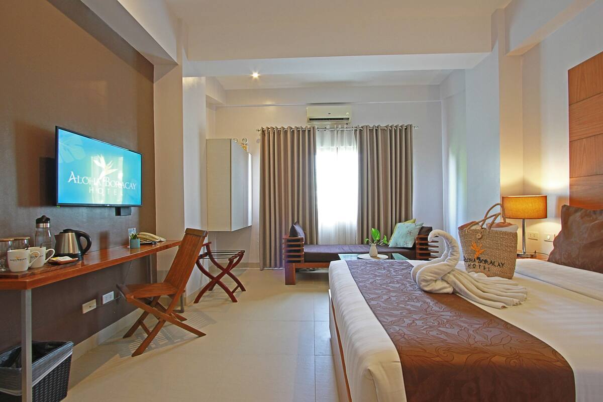 A hotel room with a bed, desk, chair, and a television displaying the hotel name.