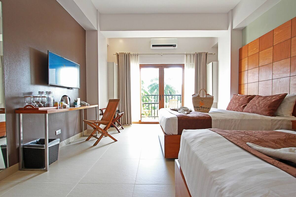 A hotel room with a bed, a desk with a TV, a chair, and a balcony with curtains.