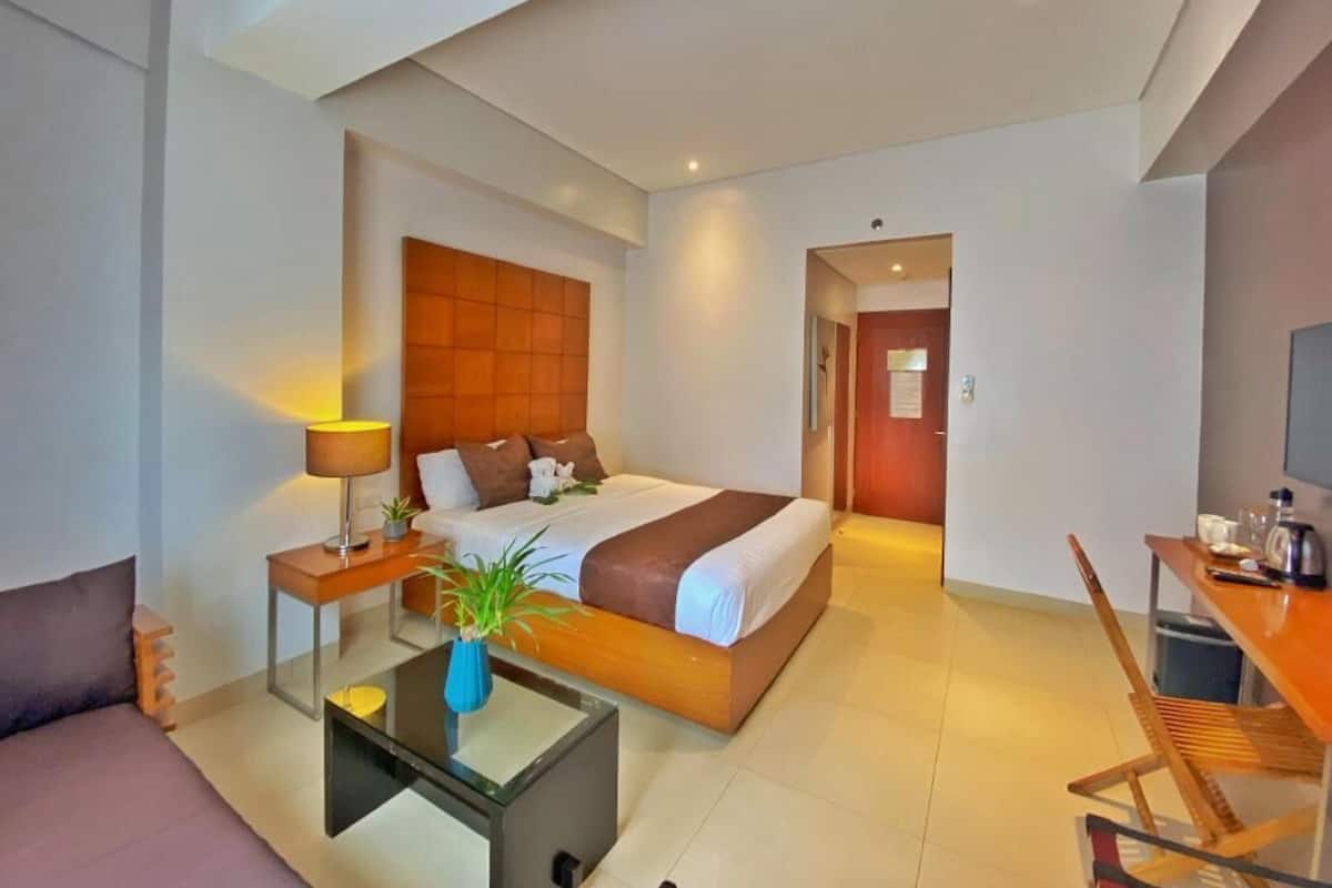 A modern hotel room with a large bed, a sitting area with a coffee table, a TV, and a desk.