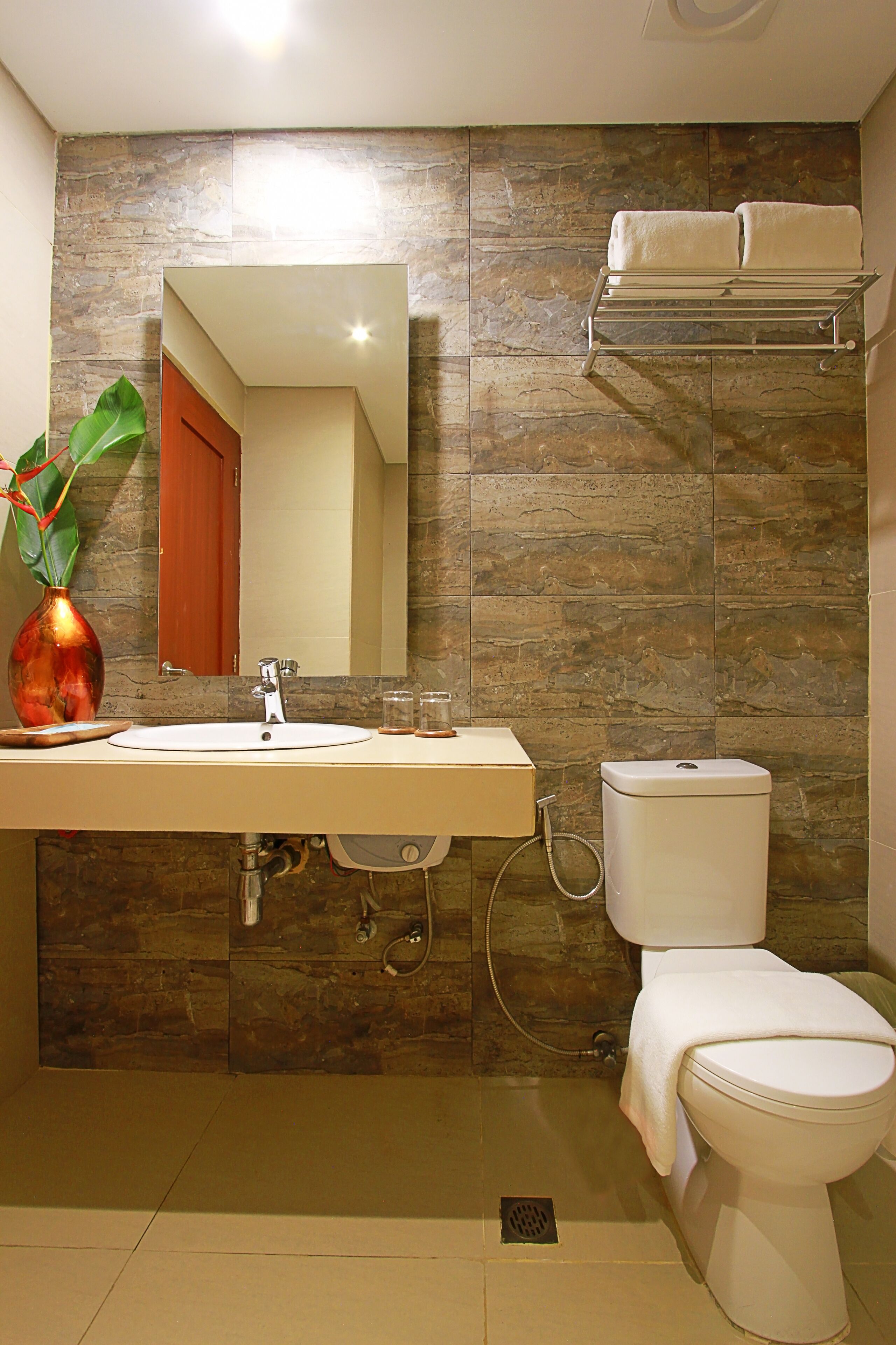 Un baño con pared de piedra, un lavamanos, un espejo, un inodoro y un perchero para toallas.