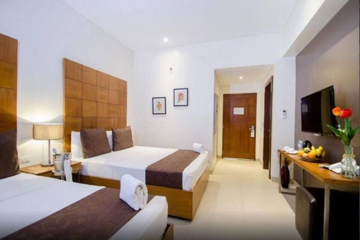 A hotel room with two beds, a desk with a flat-screen TV, and a door leading to another room.