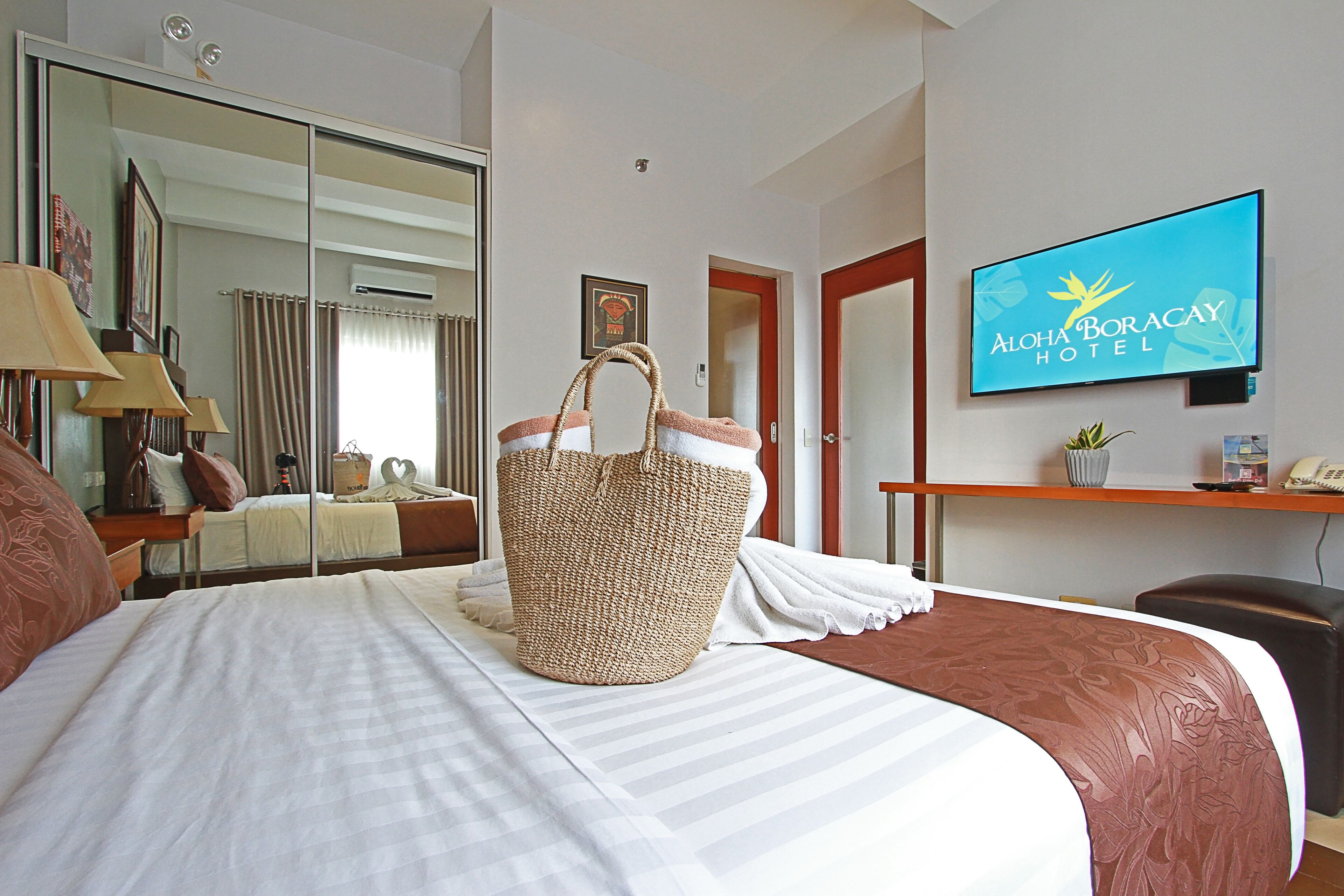 Ein Hotelzimmer mit einem Bett, einem großen gewebten Korb, einem Fernseher und einem Schreibtisch mit einer Pflanze.