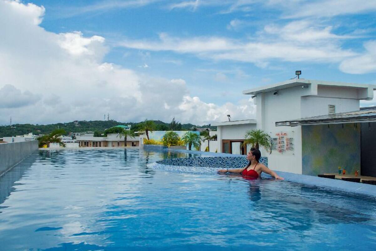 A swimming pool with a person in the water, surrounded by buildings and a clear sky.