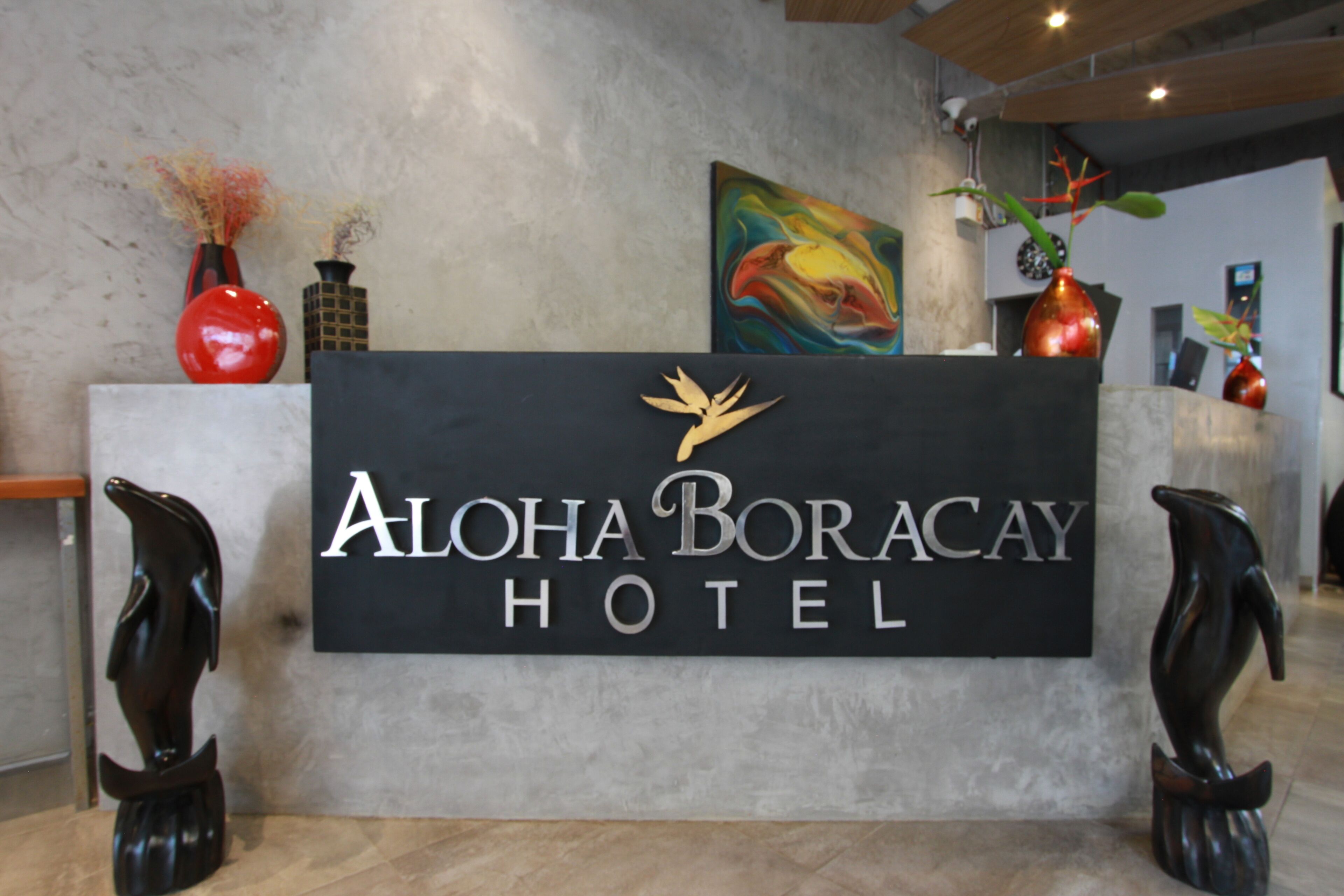 Un comptoir d’accueil avec une enseigne indiquant « Aloha Boracay Hotel », entouré de vases et de sculptures décoratives.