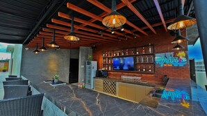 Zona de bar con una pantalla de televisión mostrando 'Space Motions', un letrero de neón que dice 'Mahaloka Sky Bar' y una variedad de botellas de licores en estantes.