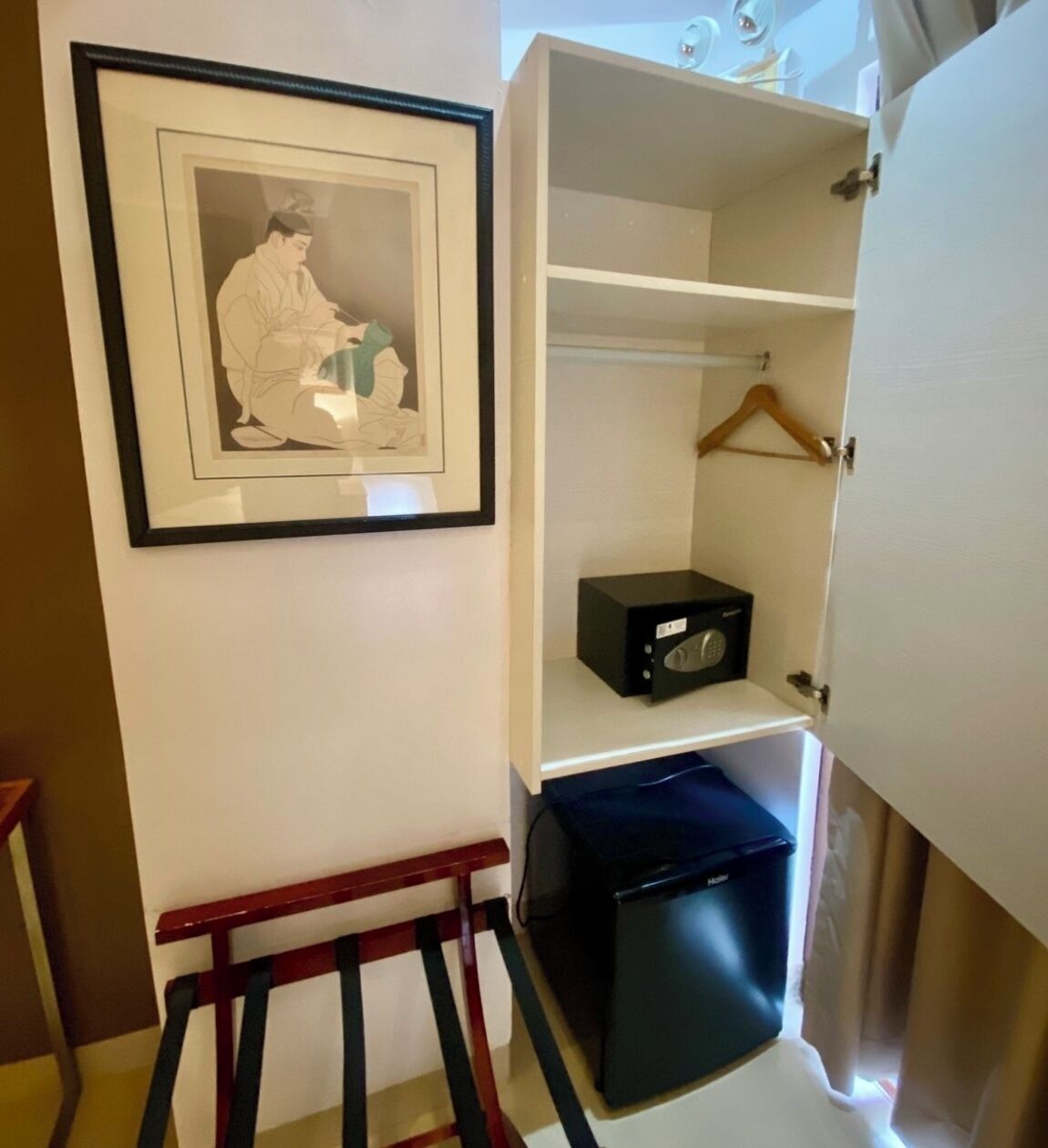 A room with a framed picture on the wall, a small black radio, and a compact black suitcase on a shelf.