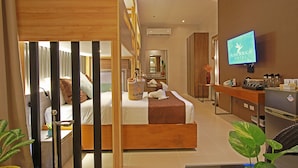 Habitación de hotel con cama, escritorio, televisión y baño visible a través de un separador.