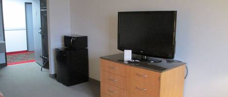 A room with a television on a wooden cabinet, a small black refrigerator, and a door leading to another room.