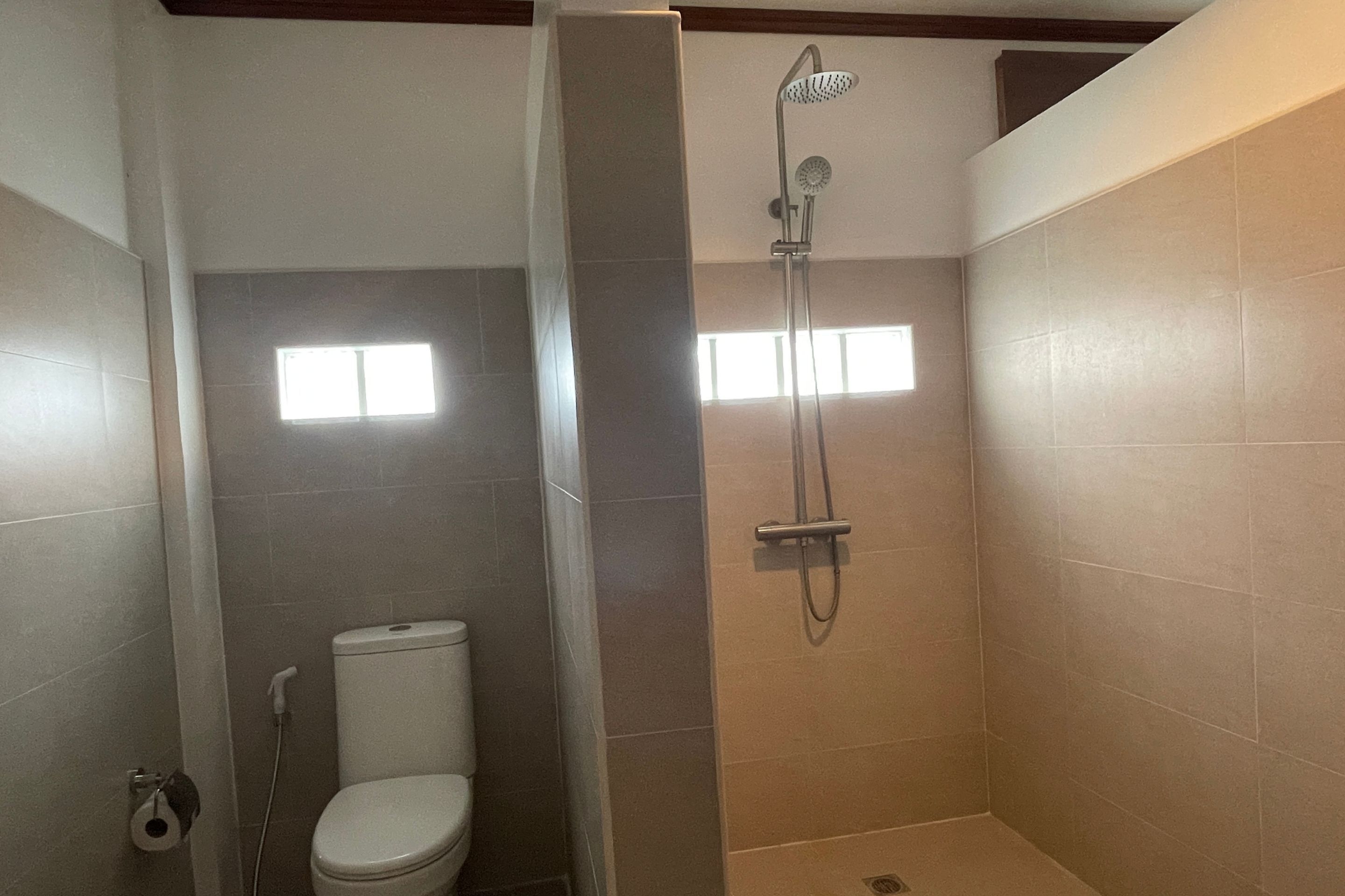 A bathroom with a shower, toilet, and a window.