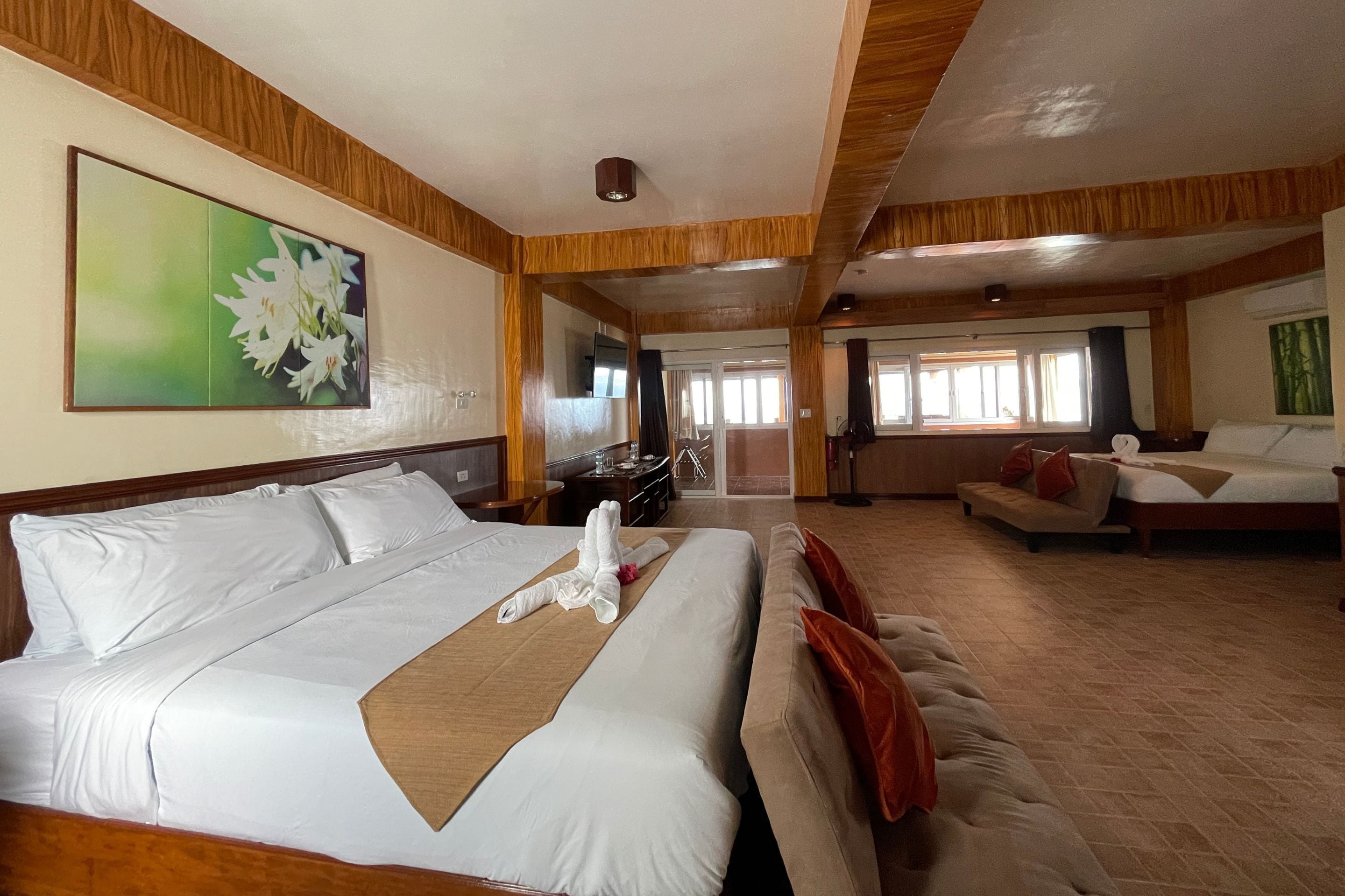 A hotel room with a large bed, a sofa, a TV, and a painting on the wall.