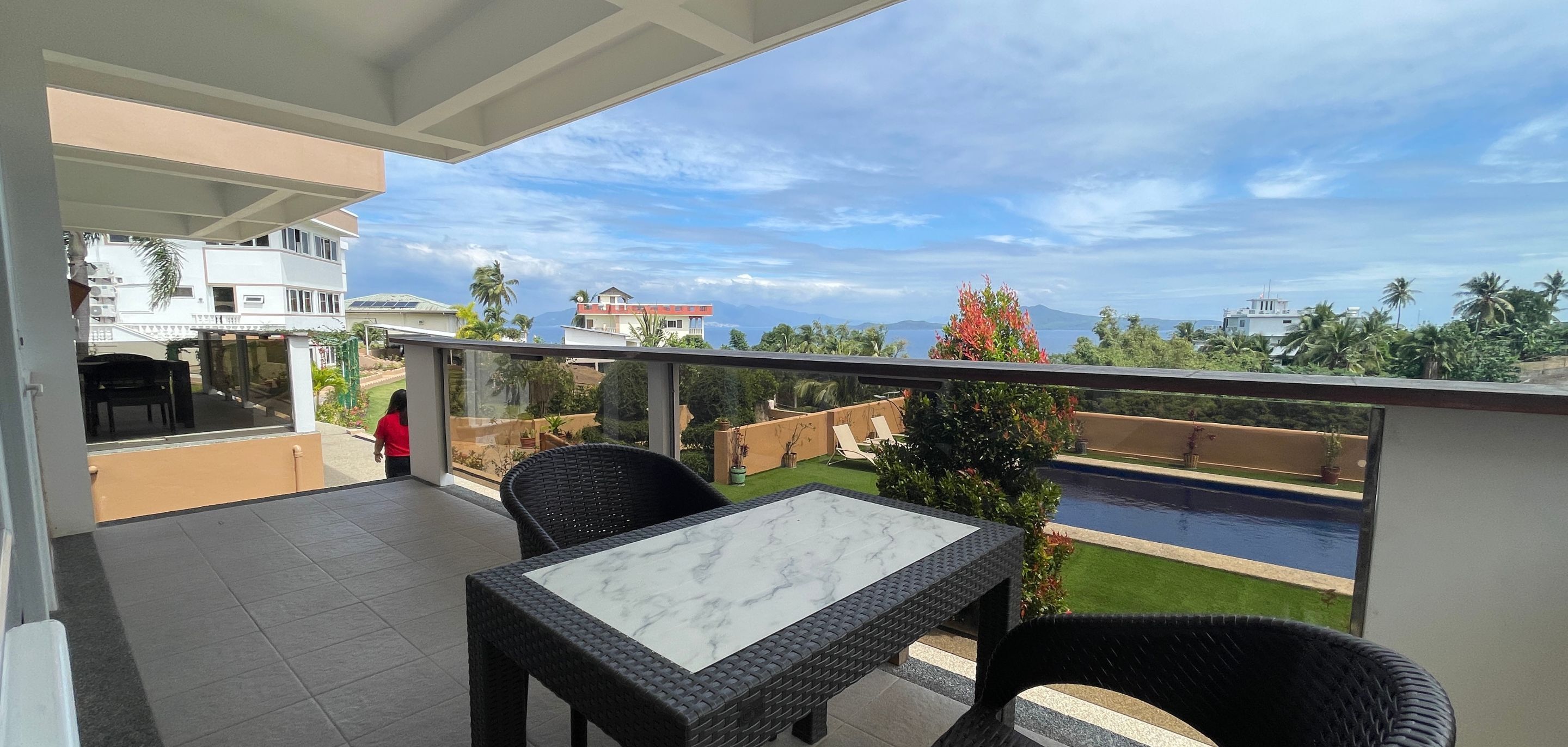 A balcony with a view of a swimming pool, a table, and chairs.