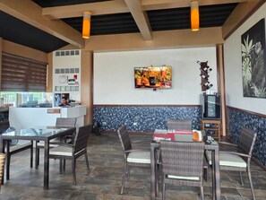 Un restaurante con terraza, un televisor en la pared y una barra con una persona detrás.