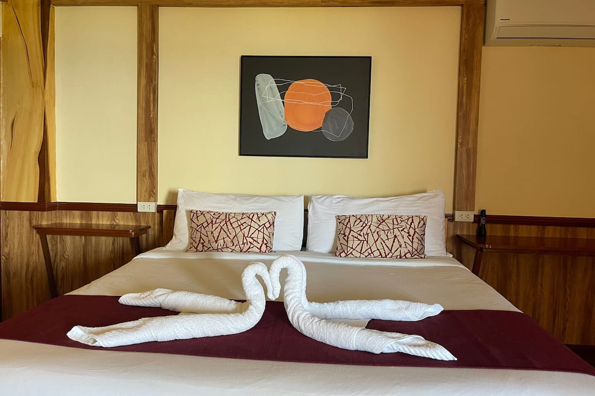 A hotel room with a bed, two pillows, a wall art piece, and towels arranged on the bed.