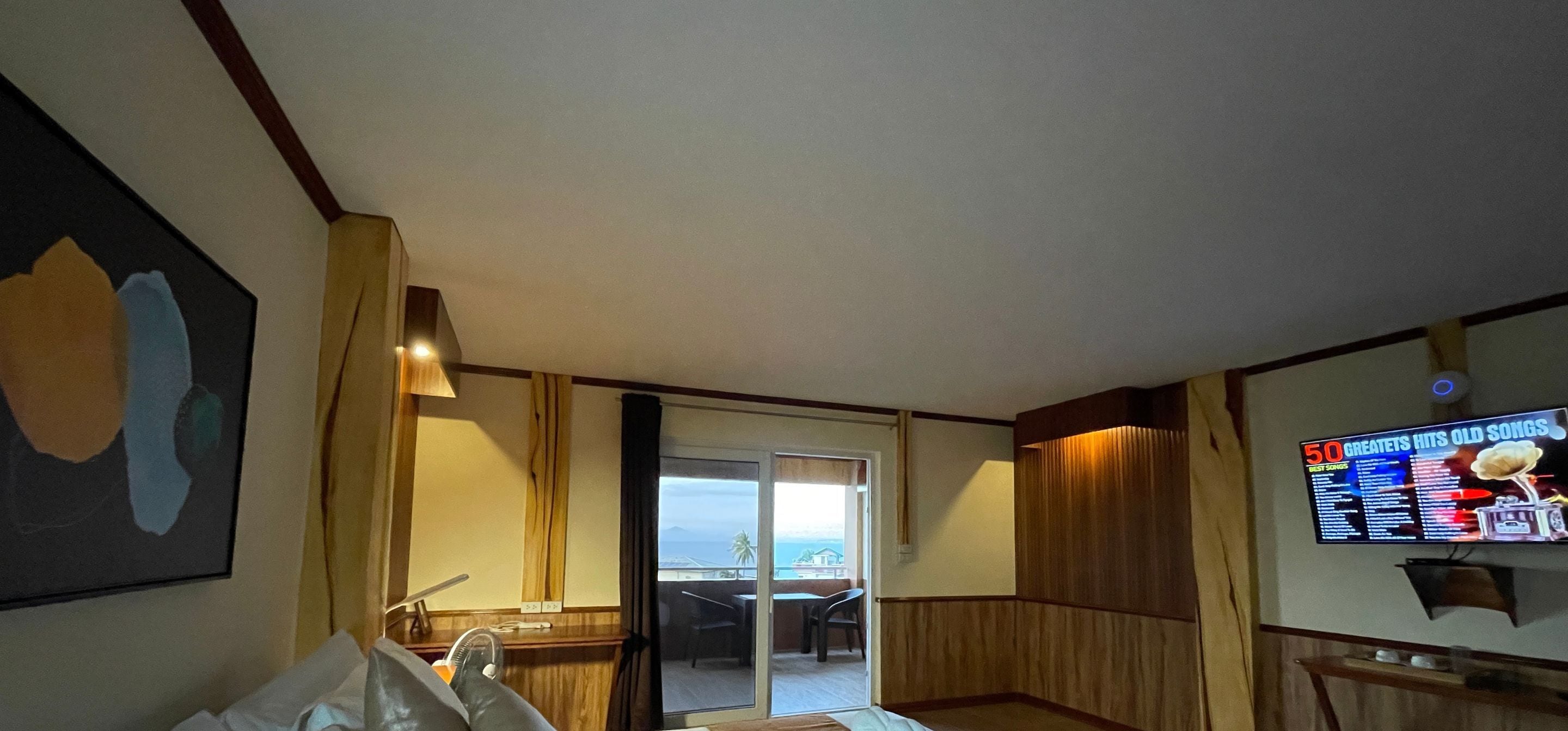 Ein Hotelzimmer mit großem Fenster, einem Flachbildfernseher, der einen Musikkanal zeigt, und Meerblick durch das Fenster.