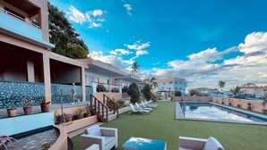 Zona junto a la piscina con césped artificial, sillas de descanso y una pequeña alberca.