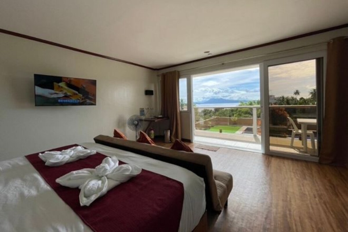 Habitación de hotel con una cama grande, un televisor de pantalla plana en la pared, un ventilador y un balcón con vistas al paisaje.