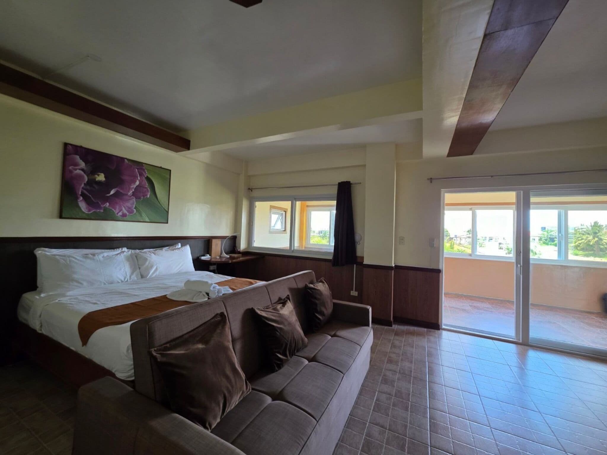 A hotel room with a large bed, a sofa, a painting, and a balcony with a view.