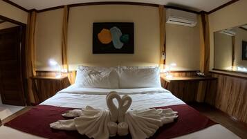 A hotel room with a neatly made bed, a heart-shaped towel arrangement, and a painting on the wall.